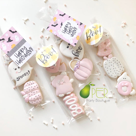 Three Halloween-themed sugar cookies packaged in clear cellophane bags with decorative tags. The cookies are decorated with pink, white, and pastel colors, featuring cute designs like a ghost, cat, pumpkin, spider, and donut.